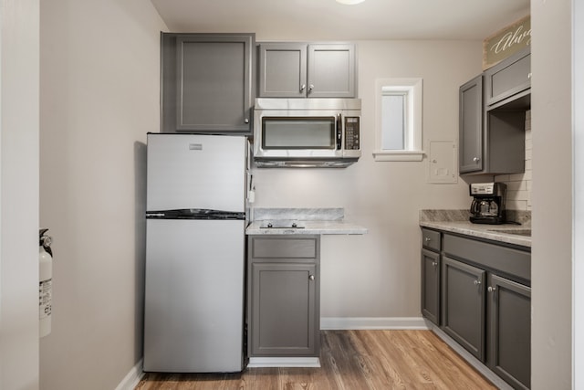 kitchen featuring stainless steel appliances, light stone counters, hardwood / wood-style floors, tasteful backsplash, and gray cabinets