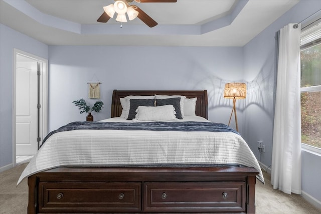 carpeted bedroom featuring multiple windows, ceiling fan, and a raised ceiling