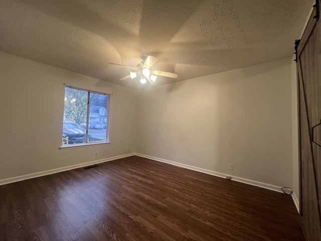 unfurnished room with ceiling fan, a barn door, dark hardwood / wood-style floors, and a textured ceiling