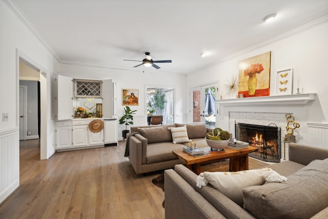 living room with light wood-type flooring, ceiling fan, a brick fireplace, and crown molding