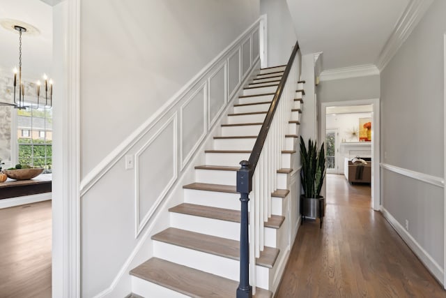 stairs with ornamental molding, hardwood / wood-style flooring, and an inviting chandelier