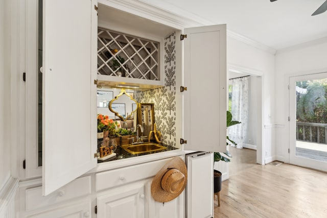 bar featuring ornamental molding, sink, light hardwood / wood-style floors, white cabinets, and ceiling fan