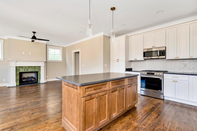 kitchen with a tile fireplace, a kitchen island, pendant lighting, white cabinets, and stainless steel appliances