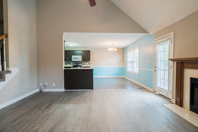 unfurnished living room with ceiling fan with notable chandelier, dark wood-type flooring, a textured ceiling, and high vaulted ceiling