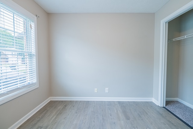 unfurnished bedroom with light hardwood / wood-style floors, multiple windows, and a closet