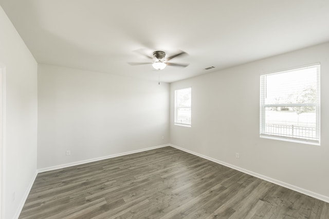 empty room with plenty of natural light, dark wood-type flooring, and ceiling fan