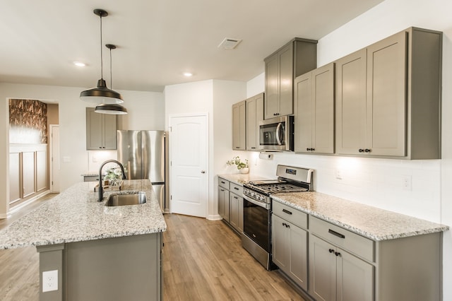 kitchen featuring stainless steel appliances, gray cabinets, hanging light fixtures, sink, and light hardwood / wood-style floors