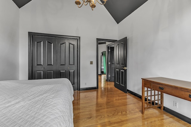 bedroom with high vaulted ceiling, wood-type flooring, a notable chandelier, and a closet