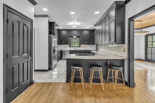 kitchen with ornamental molding, light wood-type flooring, appliances with stainless steel finishes, sink, and kitchen peninsula