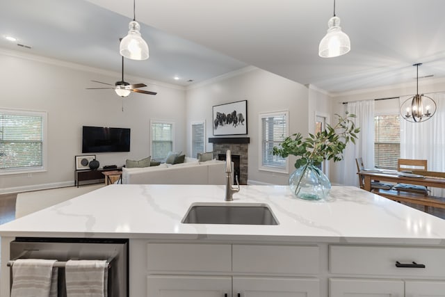 kitchen with light stone countertops, hanging light fixtures, sink, and a center island with sink