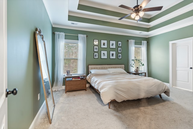 carpeted bedroom with multiple windows, ceiling fan, and a raised ceiling