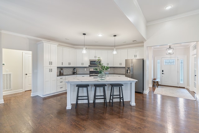 kitchen with stainless steel appliances, dark hardwood / wood-style flooring, hanging light fixtures, a kitchen island with sink, and white cabinetry