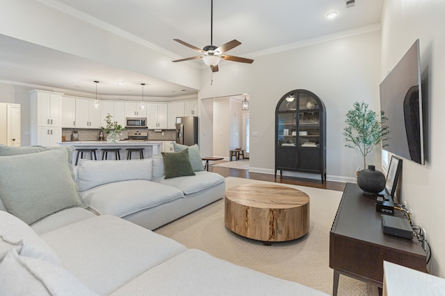 living room with light hardwood / wood-style floors, ceiling fan, a high ceiling, and crown molding