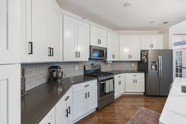 kitchen featuring backsplash, appliances with stainless steel finishes, dark hardwood / wood-style flooring, white cabinets, and dark stone countertops