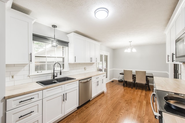 kitchen featuring stainless steel appliances, light wood-type flooring, decorative light fixtures, sink, and white cabinets