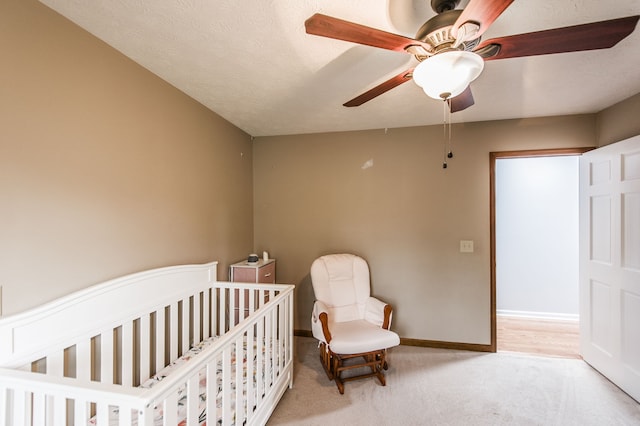 bedroom featuring ceiling fan, a textured ceiling, light carpet, and a nursery area