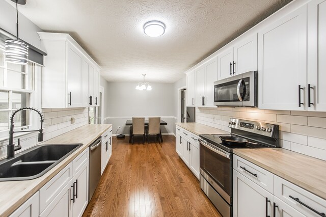 kitchen with white cabinetry, sink, appliances with stainless steel finishes, wood counters, and pendant lighting