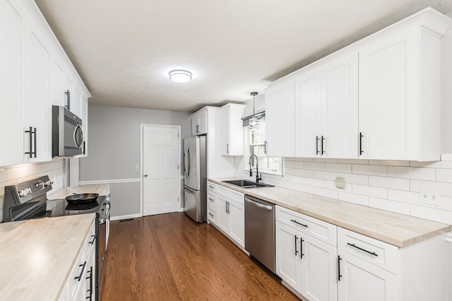 kitchen featuring butcher block counters, sink, appliances with stainless steel finishes, hanging light fixtures, and white cabinets