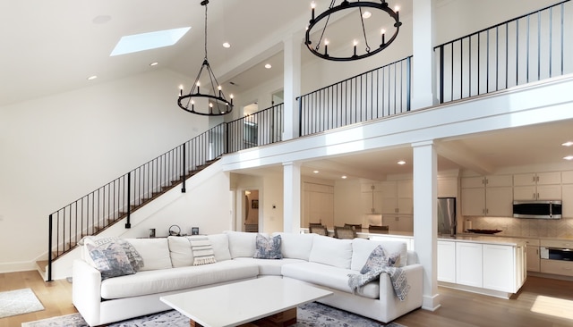 living room featuring a skylight, a towering ceiling, a notable chandelier, and light hardwood / wood-style flooring