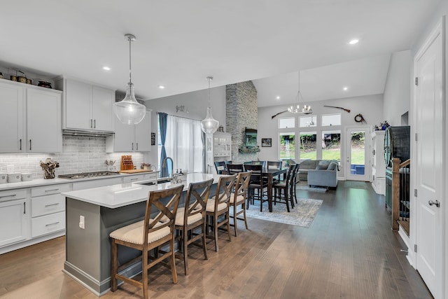 kitchen with dark wood-type flooring, white cabinets, a kitchen bar, and a kitchen island with sink