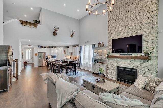 living room with wood-type flooring, a chandelier, ornamental molding, high vaulted ceiling, and a fireplace