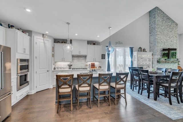 kitchen featuring a center island with sink, stainless steel appliances, white cabinetry, pendant lighting, and dark wood-type flooring