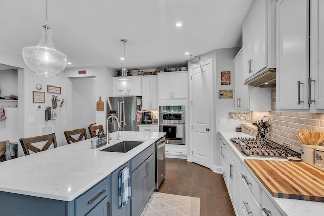 kitchen with pendant lighting, stainless steel appliances, white cabinetry, and an island with sink