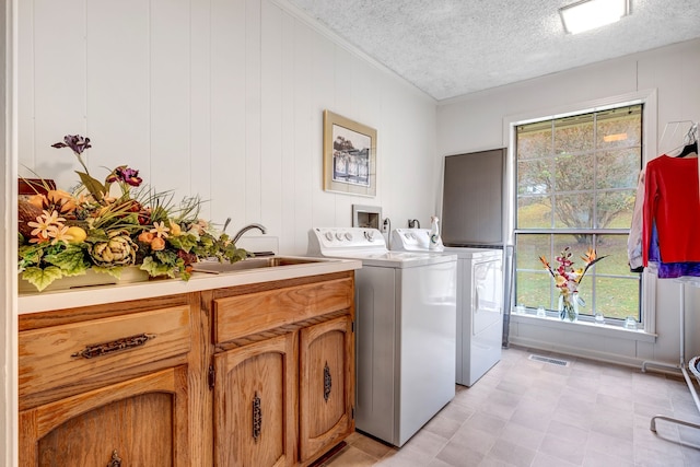 laundry room featuring a textured ceiling, separate washer and dryer, a sink, visible vents, and cabinet space