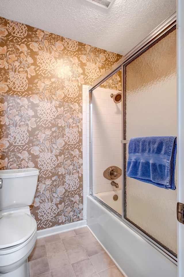 bathroom featuring a textured ceiling, combined bath / shower with glass door, baseboards, and wallpapered walls