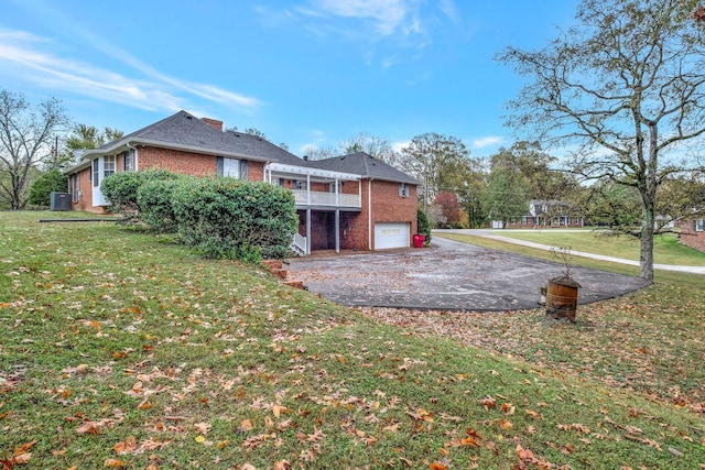 back of property with a garage, driveway, brick siding, and a lawn