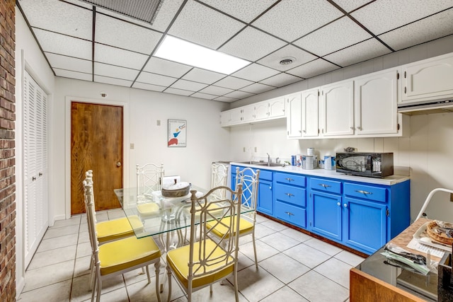 kitchen with black microwave, blue cabinetry, a drop ceiling, and light tile patterned floors