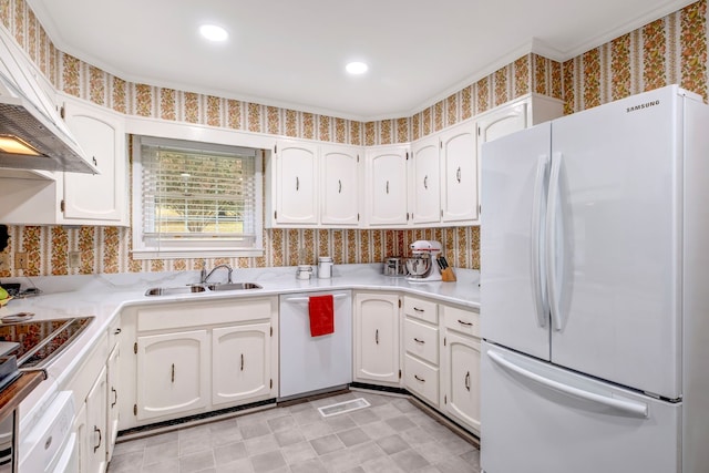 kitchen with light countertops, white cabinets, a sink, white appliances, and wallpapered walls