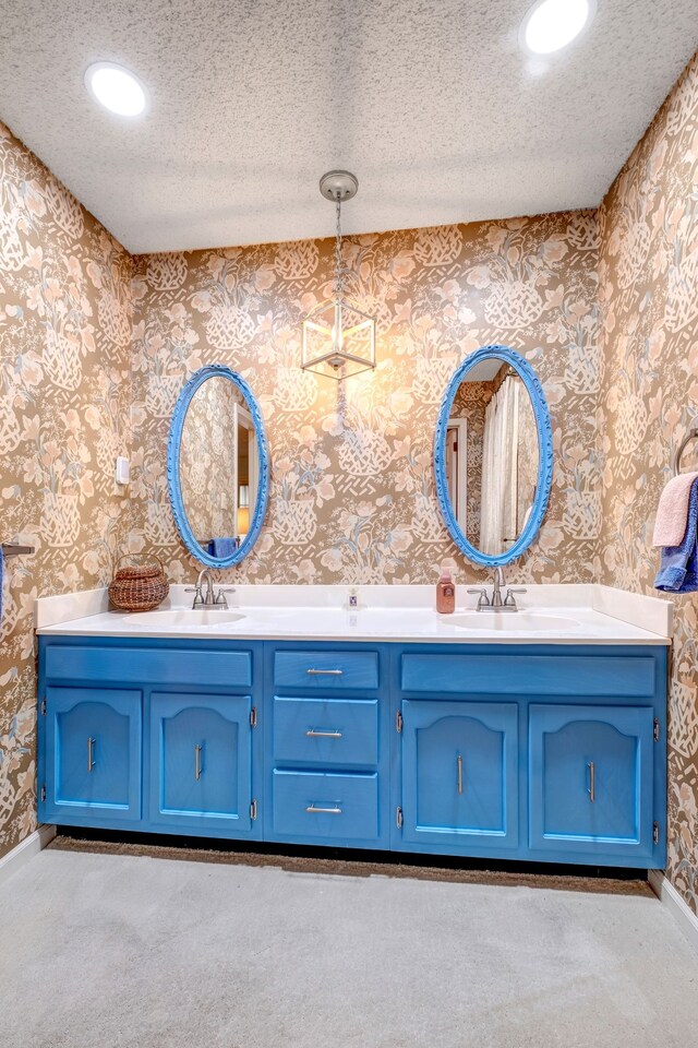 bathroom featuring a textured ceiling, a sink, and wallpapered walls