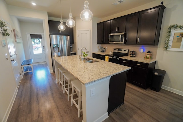 kitchen with dark wood-type flooring, sink, a kitchen island with sink, light stone countertops, and appliances with stainless steel finishes