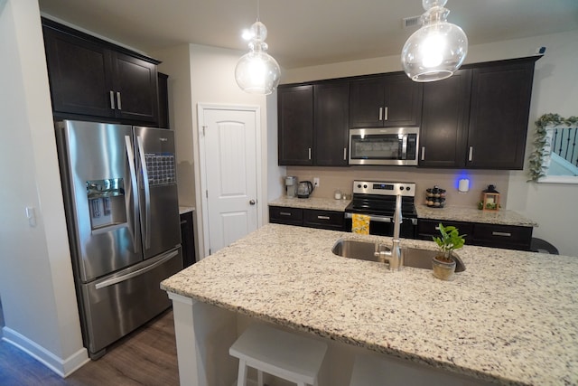 kitchen featuring sink, light stone counters, appliances with stainless steel finishes, hanging light fixtures, and dark hardwood / wood-style flooring