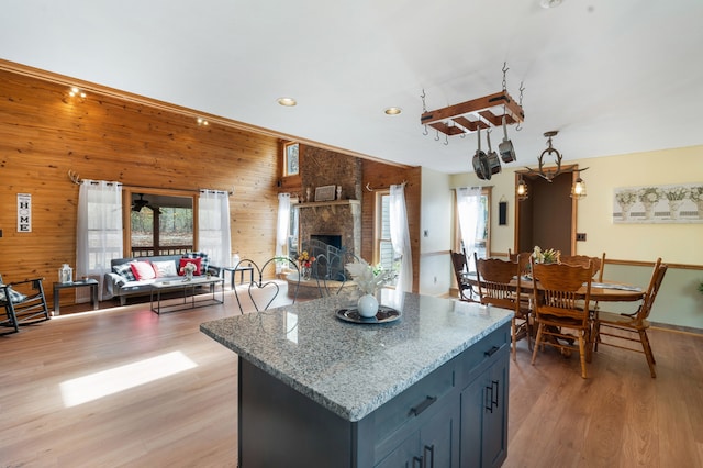 kitchen with wood walls, light stone counters, high vaulted ceiling, a stone fireplace, and light hardwood / wood-style flooring