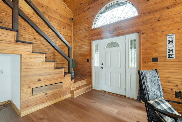 foyer with wood-type flooring, wooden walls, and high vaulted ceiling