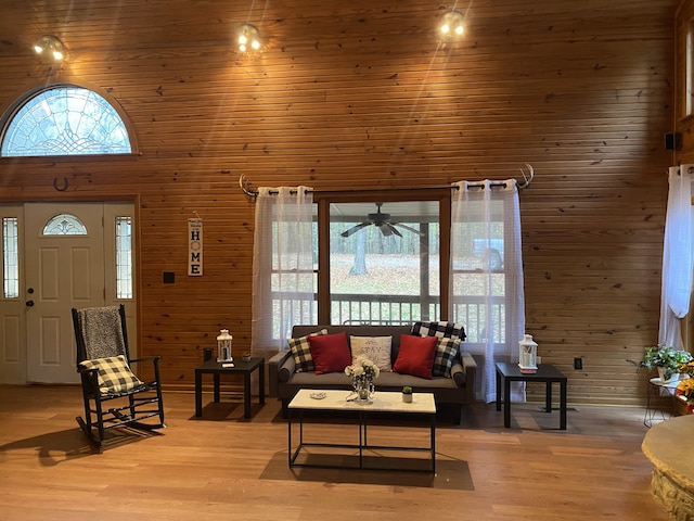 living room featuring a wealth of natural light, wood-type flooring, wooden walls, and a towering ceiling