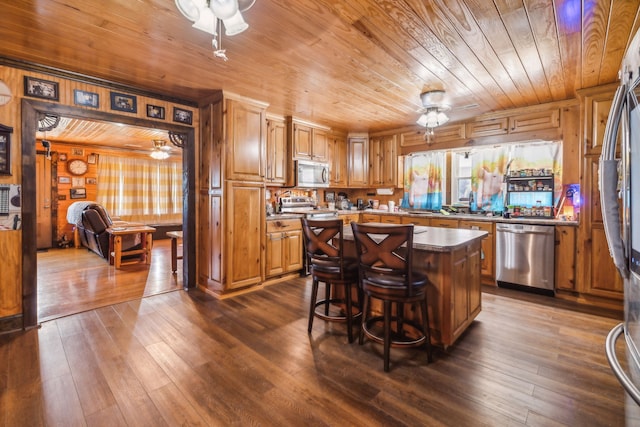 kitchen featuring dark wood-type flooring, wooden walls, appliances with stainless steel finishes, and a center island