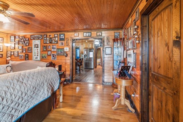 bedroom featuring stainless steel refrigerator with ice dispenser, wood walls, wooden ceiling, and wood-type flooring