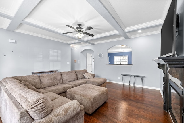 living room featuring dark wood-type flooring, coffered ceiling, ceiling fan with notable chandelier, ornamental molding, and beamed ceiling