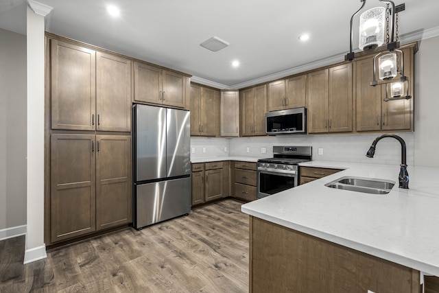 kitchen featuring crown molding, appliances with stainless steel finishes, decorative light fixtures, sink, and dark wood-type flooring