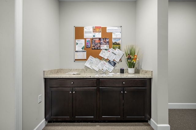 bar with dark brown cabinetry, carpet floors, and light stone counters