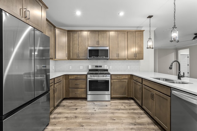 kitchen featuring stainless steel appliances, kitchen peninsula, hanging light fixtures, sink, and light hardwood / wood-style flooring