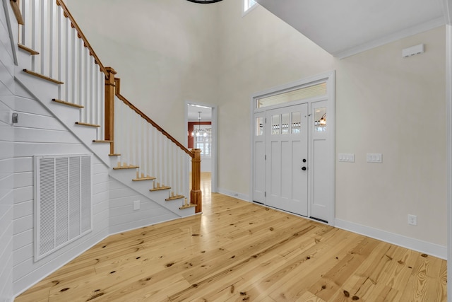 entrance foyer with hardwood / wood-style floors, a towering ceiling, and crown molding