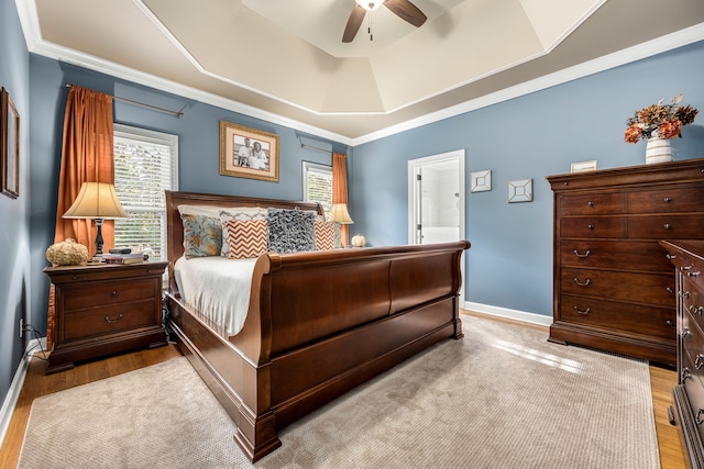 bedroom with ensuite bath, ornamental molding, ceiling fan, a tray ceiling, and light hardwood / wood-style flooring