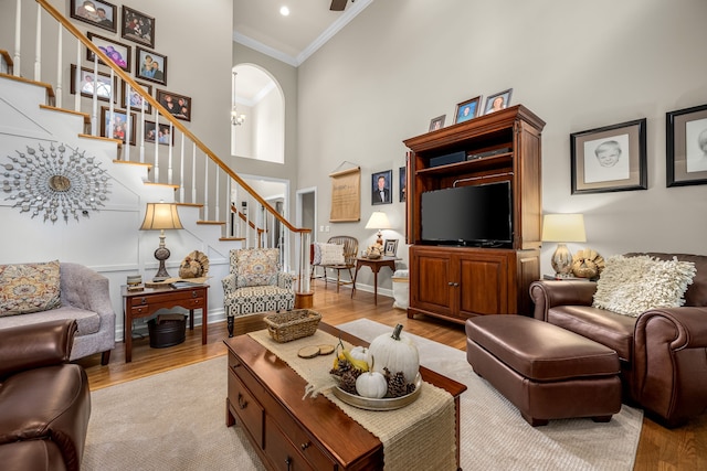 living room featuring light wood-type flooring, ornamental molding, and a towering ceiling