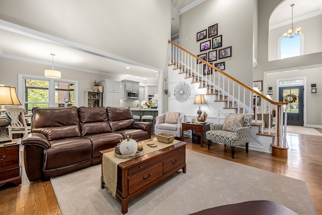 living room with an inviting chandelier, a towering ceiling, crown molding, and light hardwood / wood-style flooring