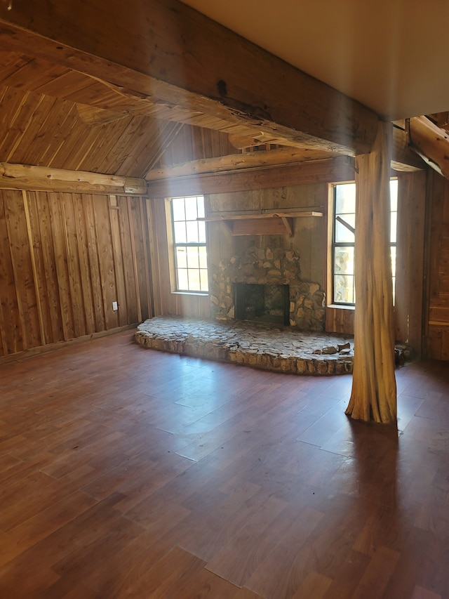 unfurnished living room with dark hardwood / wood-style flooring, wooden walls, wooden ceiling, and a stone fireplace