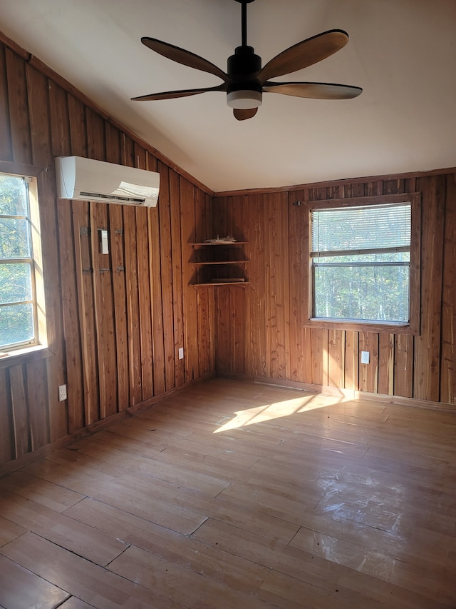 unfurnished room featuring light wood-type flooring, ceiling fan, wooden walls, and an AC wall unit